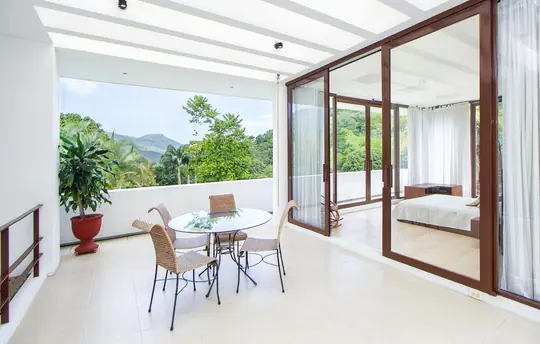 Galería acristalada en terraza reformada con mesa, sillas y vistas a vegetación tropical