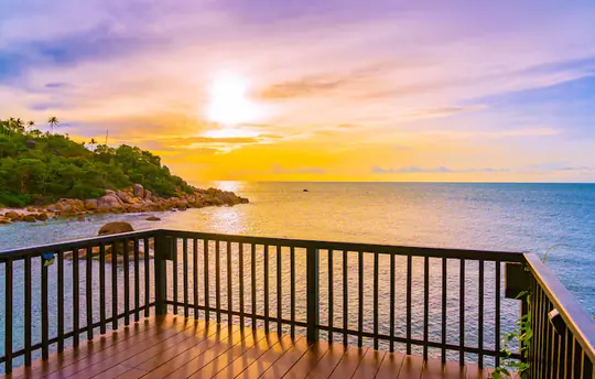 Balcón de madera reformado con barandilla de hierro y vistas al mar tropical al atardecer