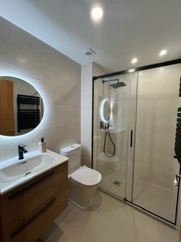 Bany reformat a Girona amb lavabo de fusta, espill rodó amb llum LED i mampara de vidre amb perfil negre