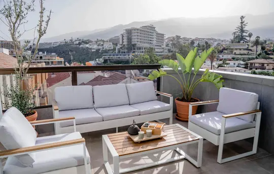 Terrassa reformada amb zona lounge de sofàs blancs, jardinera i vistes panoràmiques a la ciutat