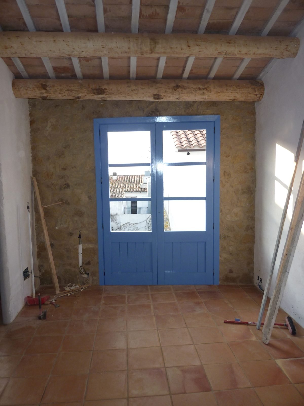 Habitación de la casa reformada en Calella de Palafrugell con balconera azul, vigas de madera y suelo de barro cocido