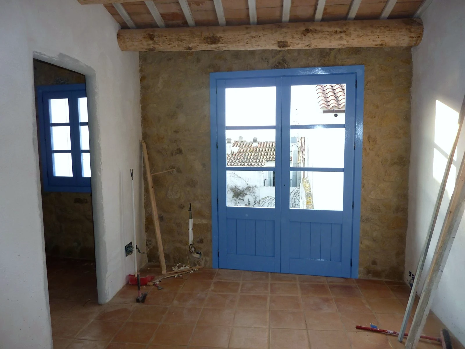 Habitació amb balconera blava, bigues de fusta i terra de terra cuita