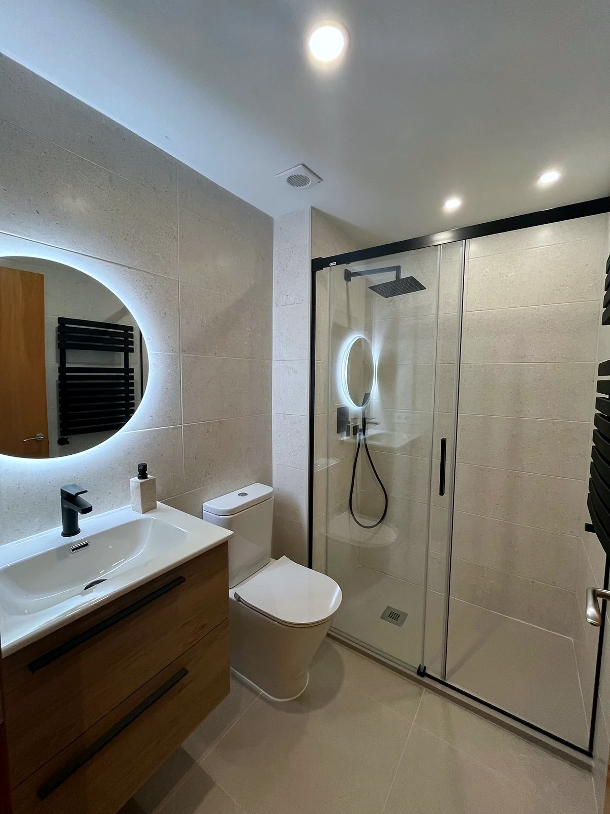 Moble de lavabo de fusta suspès i dutxa amb mampara de vidre al bany reformat