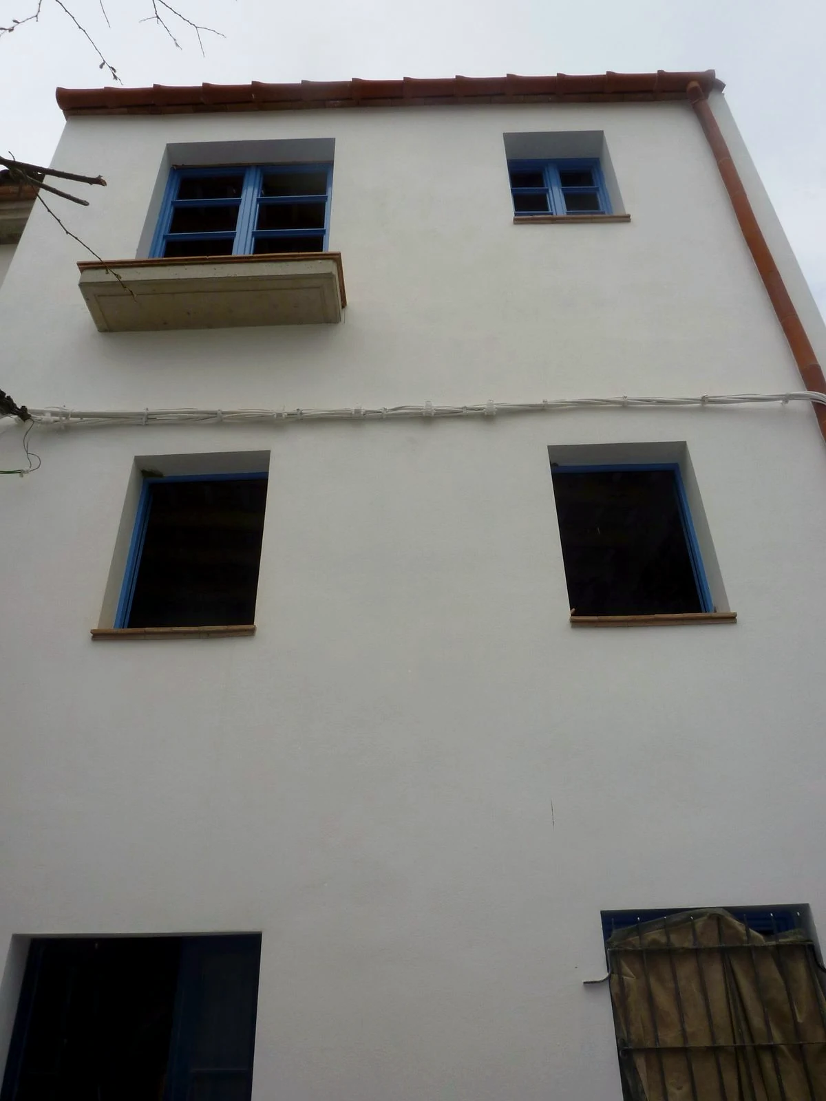 Façana blanca acabada amb finestres blaves i balcó després de la reforma de la casa a Calella de Palafrugell